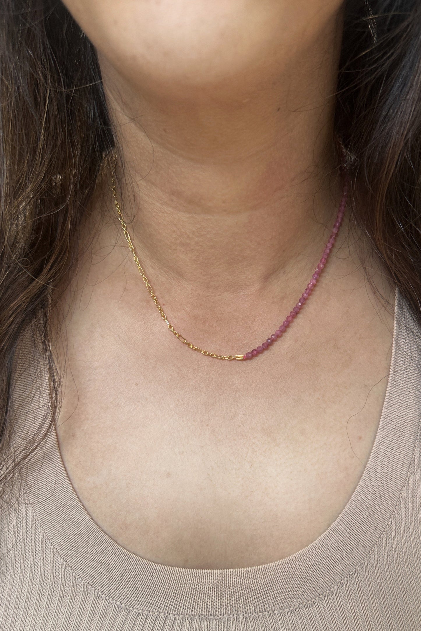 Person wearing a gold necklace with a pink stone