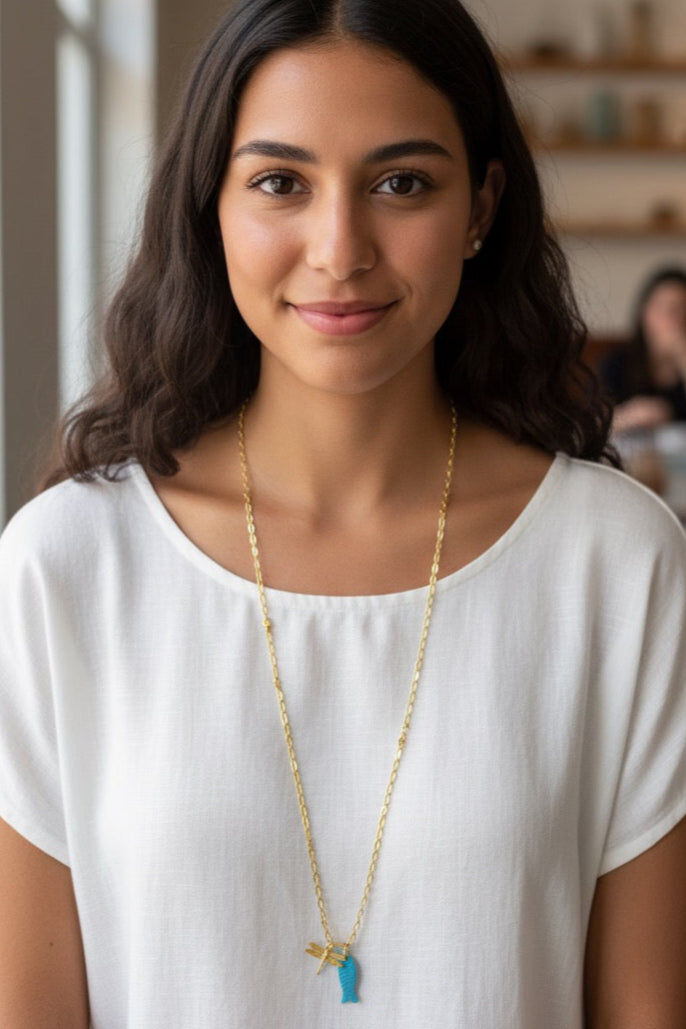 Woman wearing a white top and gold necklace with a blue pendant indoors.