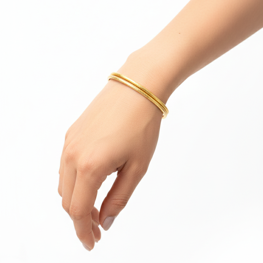 Gold bangles on a hand against a white background