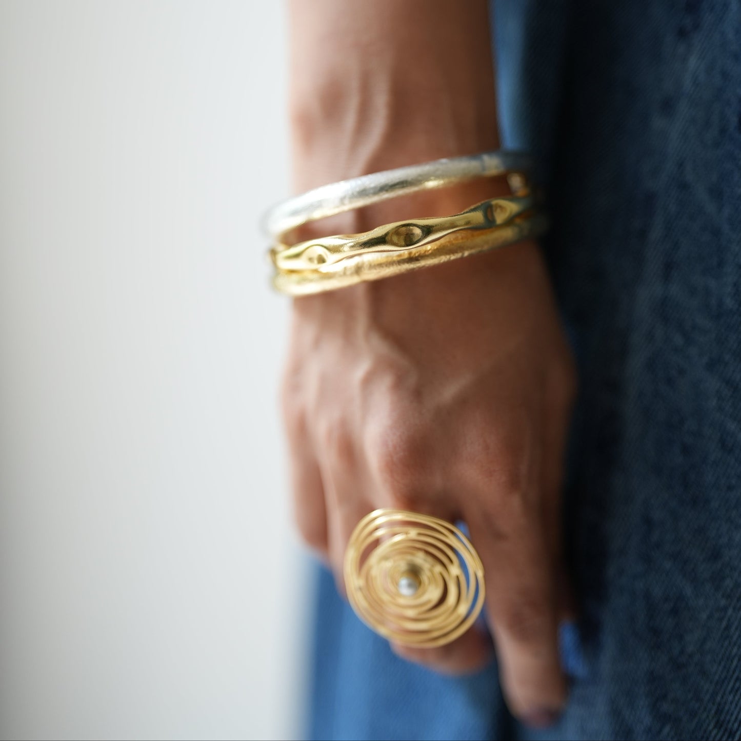 Hand wearing gold rings and bracelets on a blue fabric background
