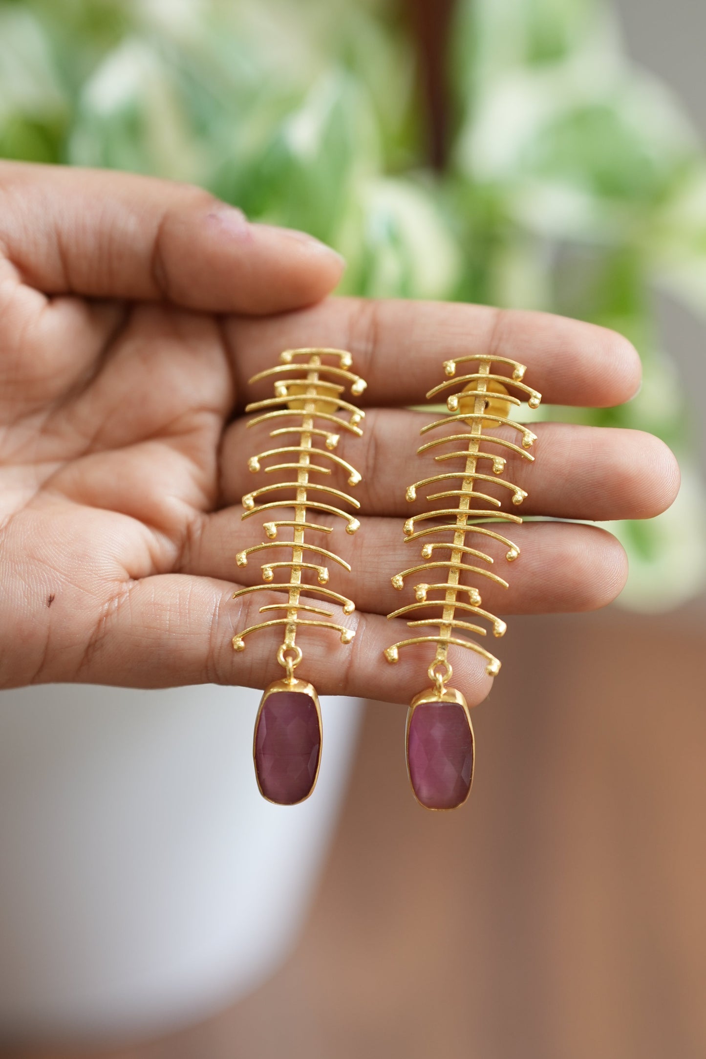Hand holding gold and pink fishbone-shaped earrings.