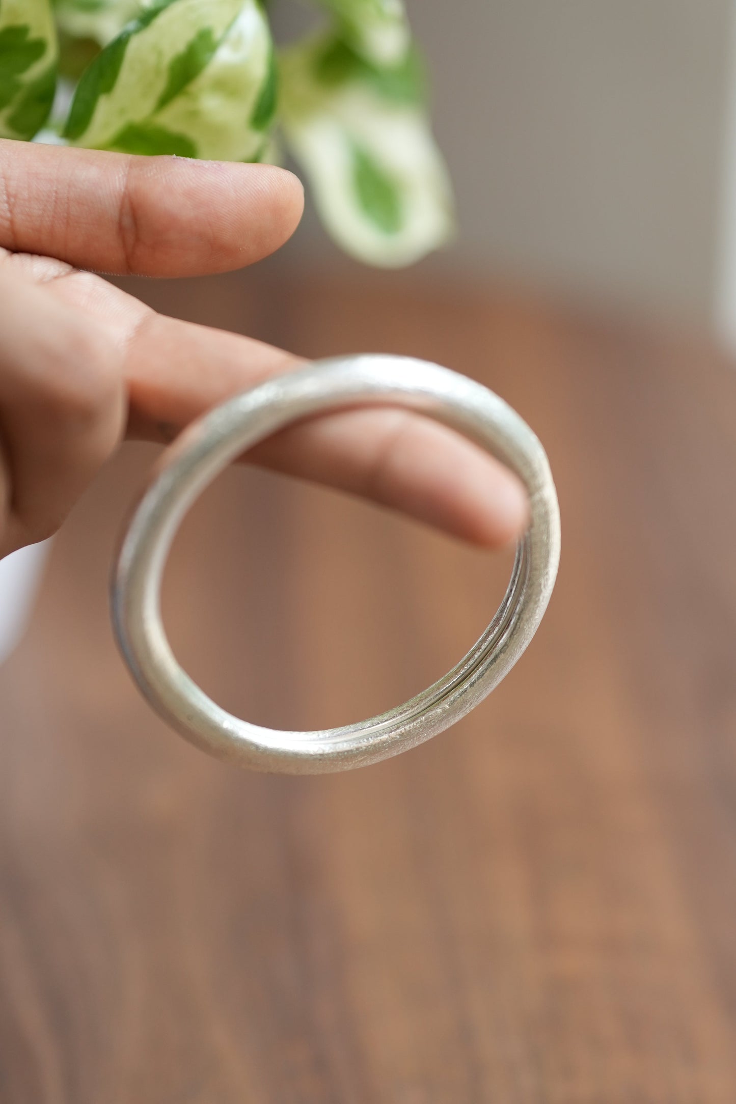 Hand holding a silver ring against a wooden background