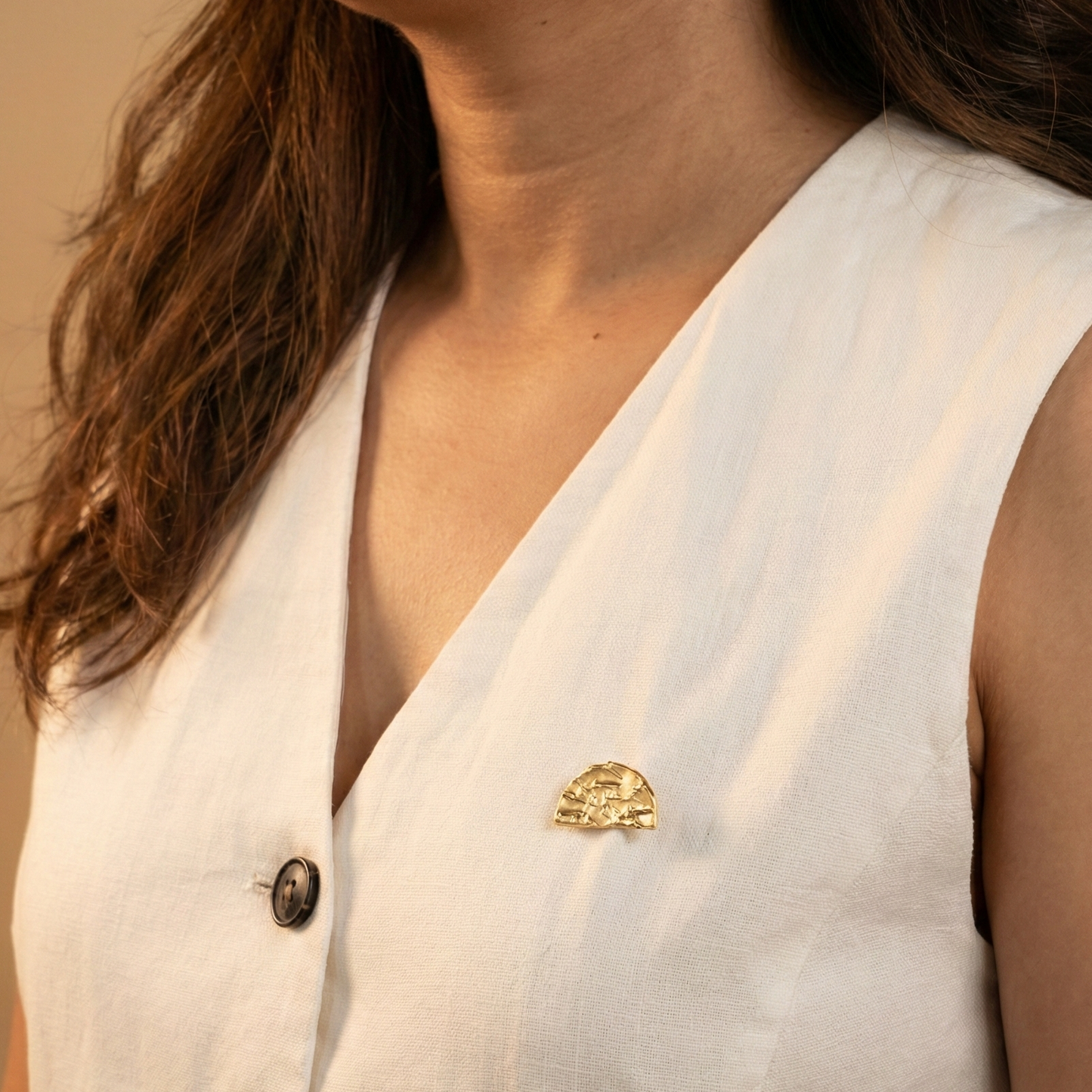 Close-up of a person wearing a white sleeveless top with a gold brooch and buttons.