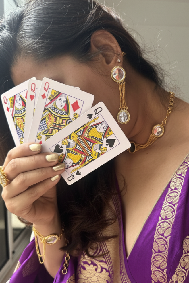 Woman in a purple saree holding playing cards in front of her face.