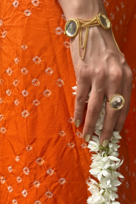 Person wearing an orange saree with floral patterns, holding a white flower garland, in an indoor setting.