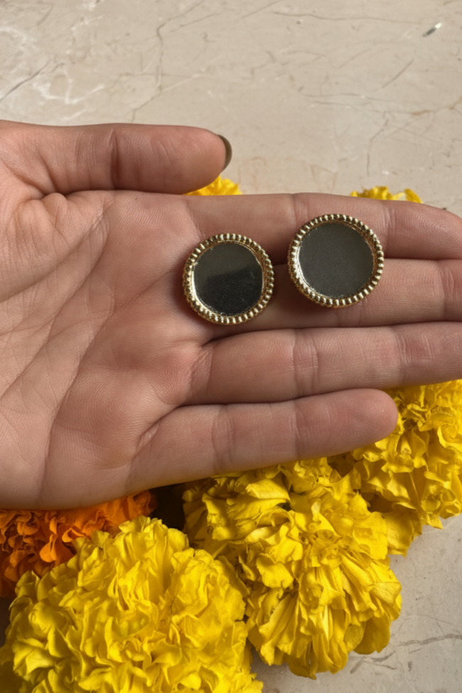 Gold-framed black circular objects held between yellow flowers on a light-colored surface.