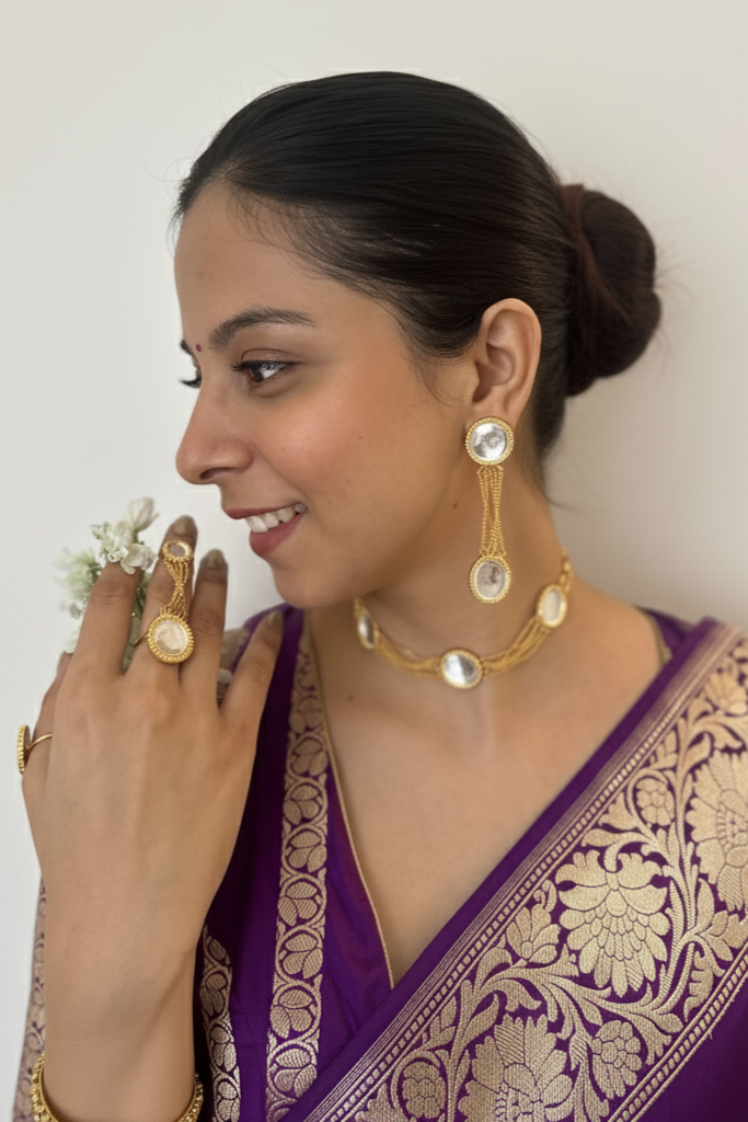 Woman wearing a purple saree with gold jewelry against a white background