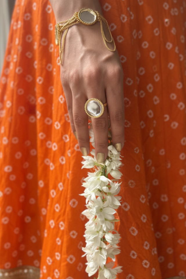 Person wearing an orange traditional outfit with a gold bracelet and ring, holding a white flower garland.