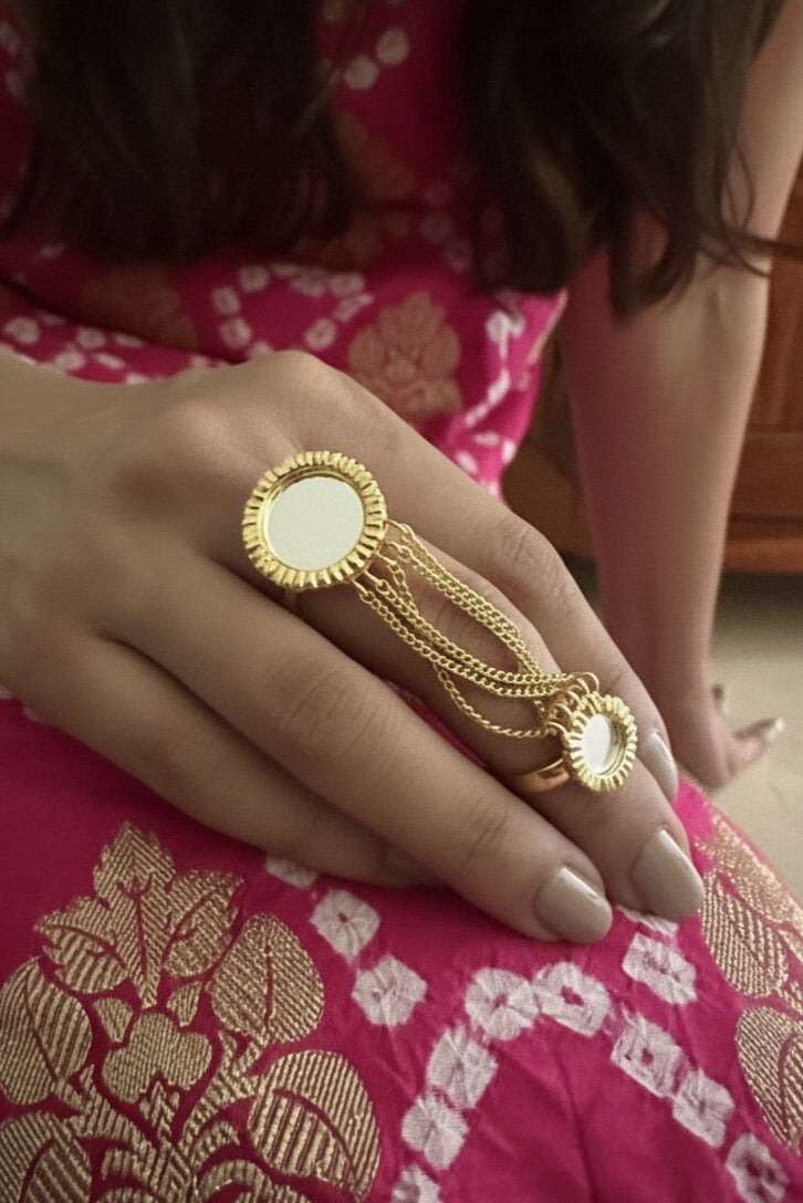 Close-up of a hand wearing a gold ring with a circular design on a pink fabric background.