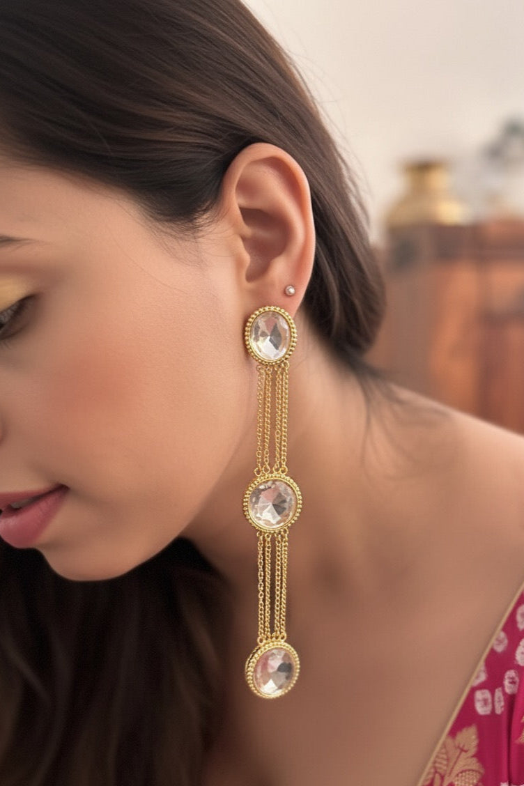 Woman wearing gold earrings with clear gemstones, blurred background