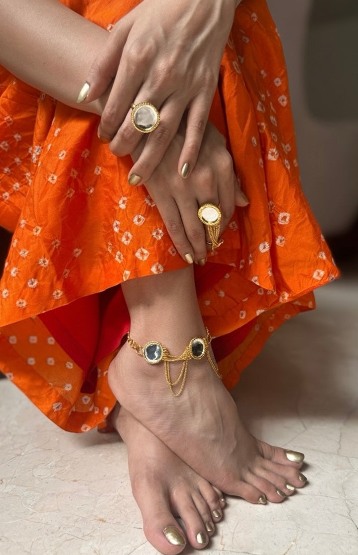 Close-up of a person's feet wearing gold anklets and rings, with an orange garment.