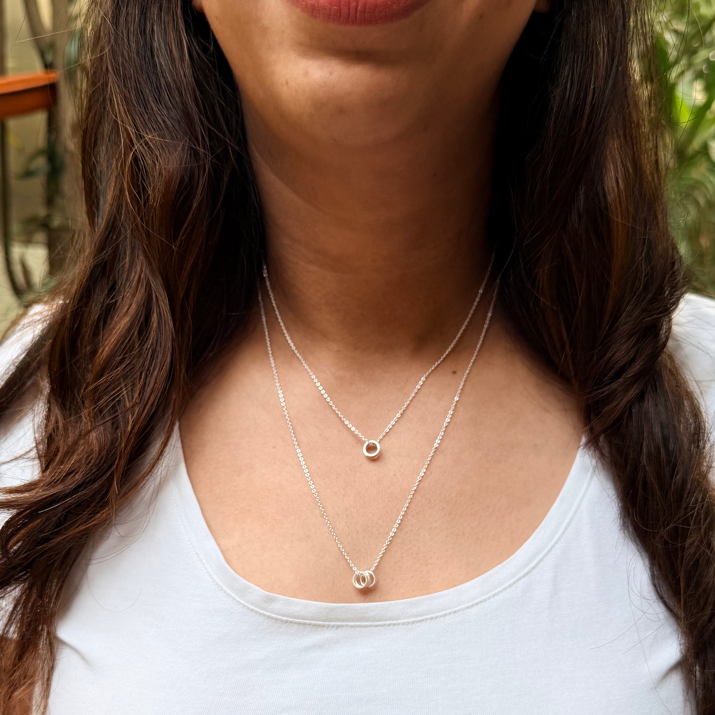 Woman wearing a white tank top with necklaces, standing outdoors.