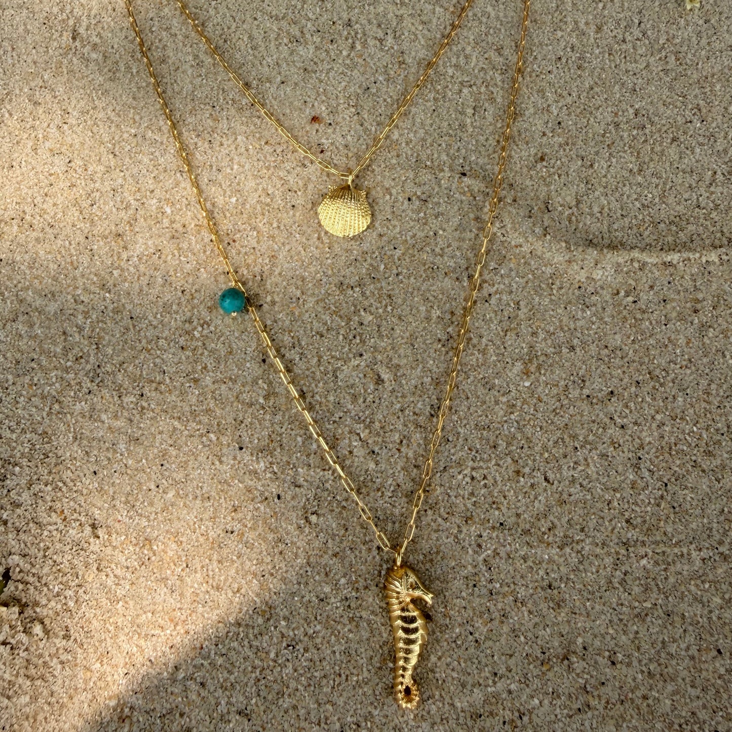 Gold necklace with a seahorse and shell pendant .