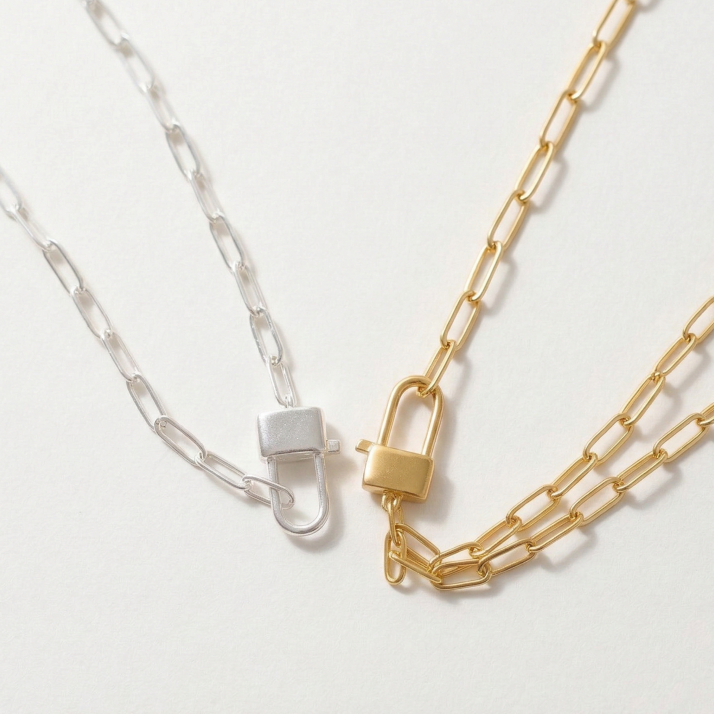 Two chain necklaces, one gold and one silver, on a light gray background.