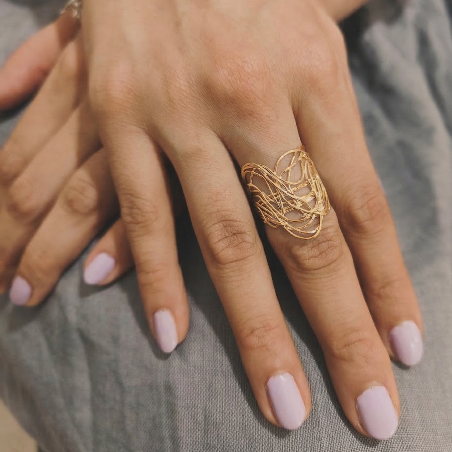 Hand wearing a gold ring with pink nail polish on a neutral background