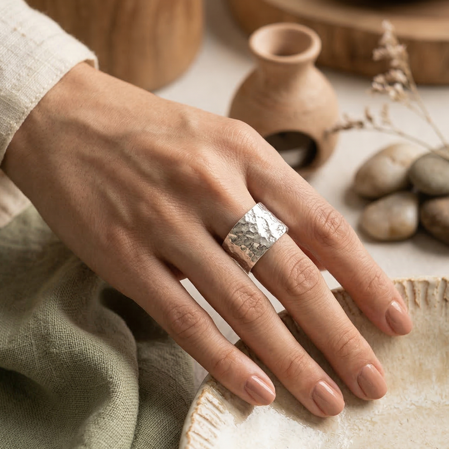Hand wearing a silver ring with natural elements in the background