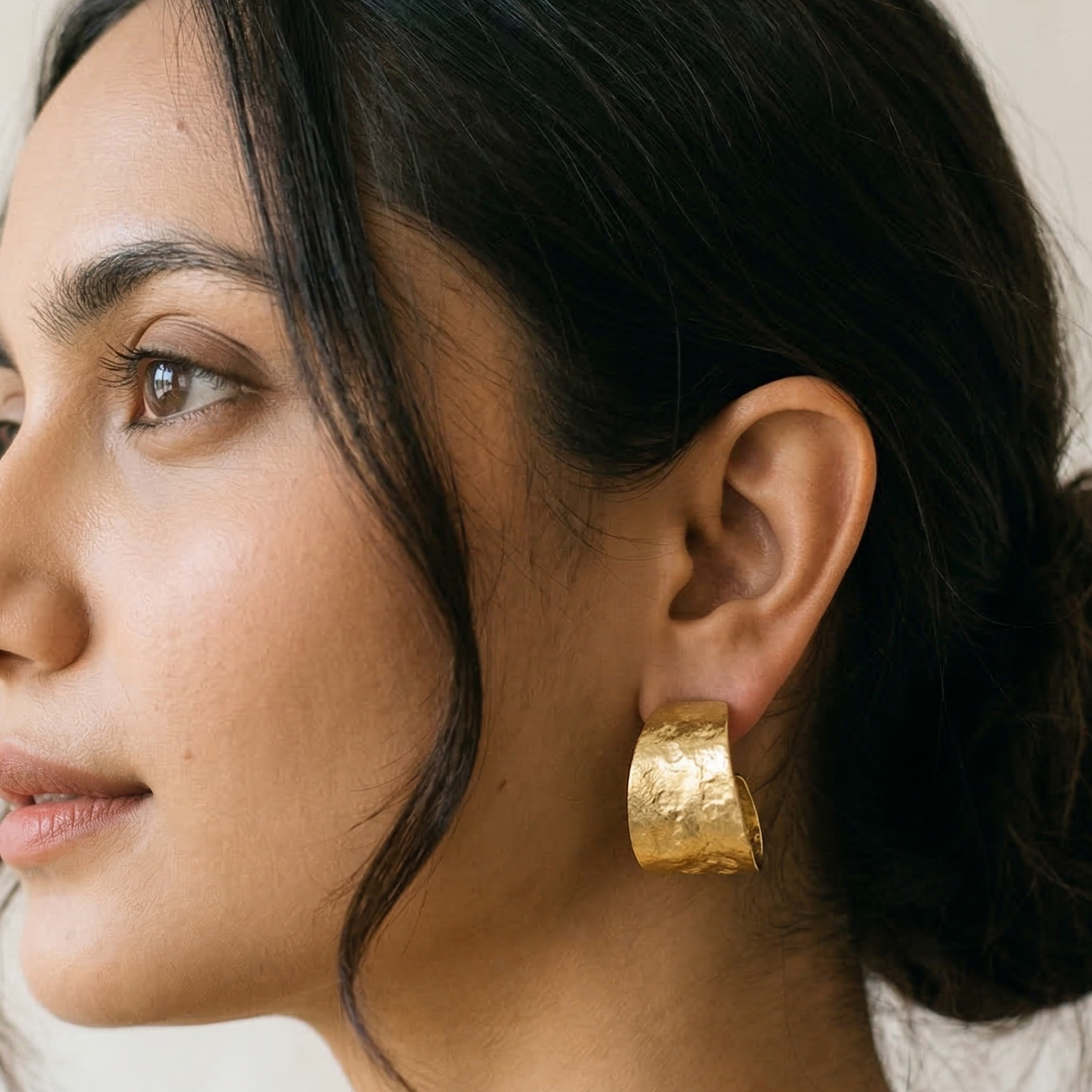 Woman wearing gold hoop earrings with a neutral background