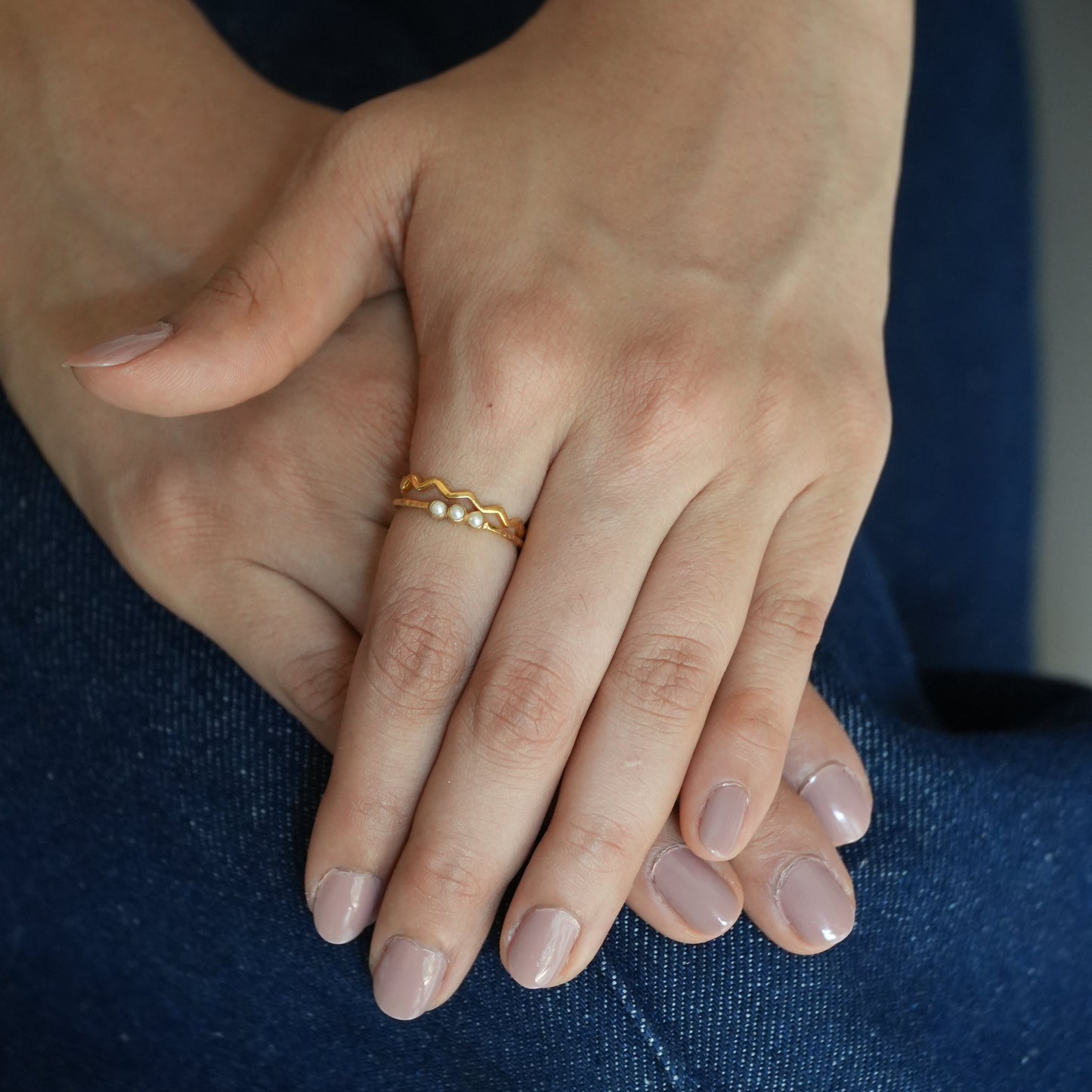 Close-up of a hand wearing a gold ring with a blue fabric background