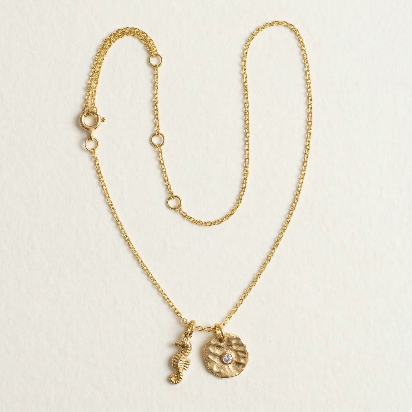 Gold necklace with two charms on a light beige background