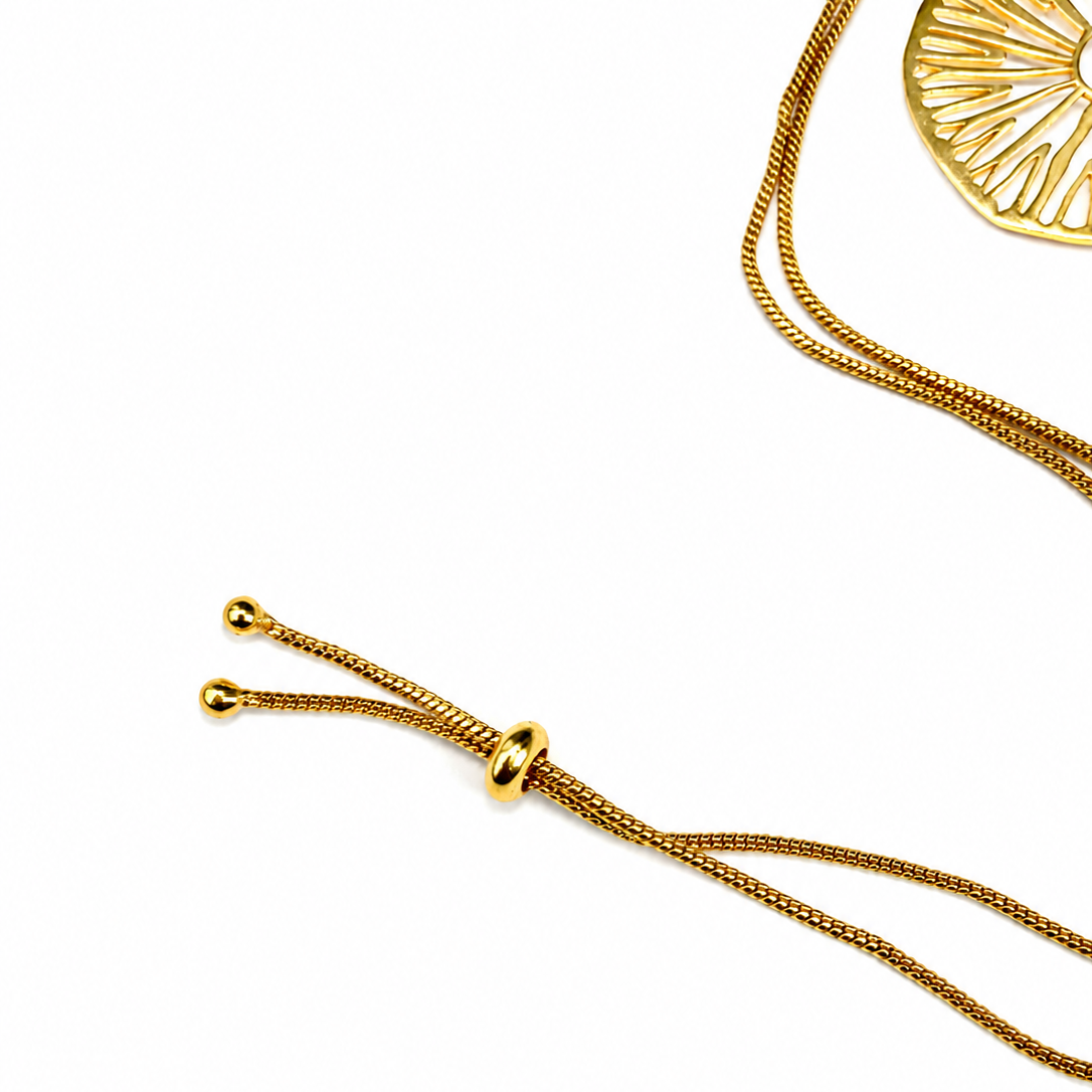 Close-up of a gold adjustable necklace with a textured snake chain, a sliding bead closure, and a partially visible round gold pendant on a white background.