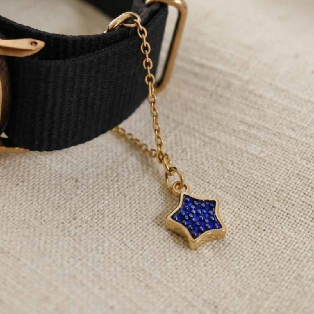 Black watch with gold chain and blue star charm on a beige fabric background