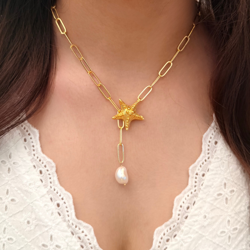 Gold necklace with a star and pearl pendant worn by a person with long dark hair.