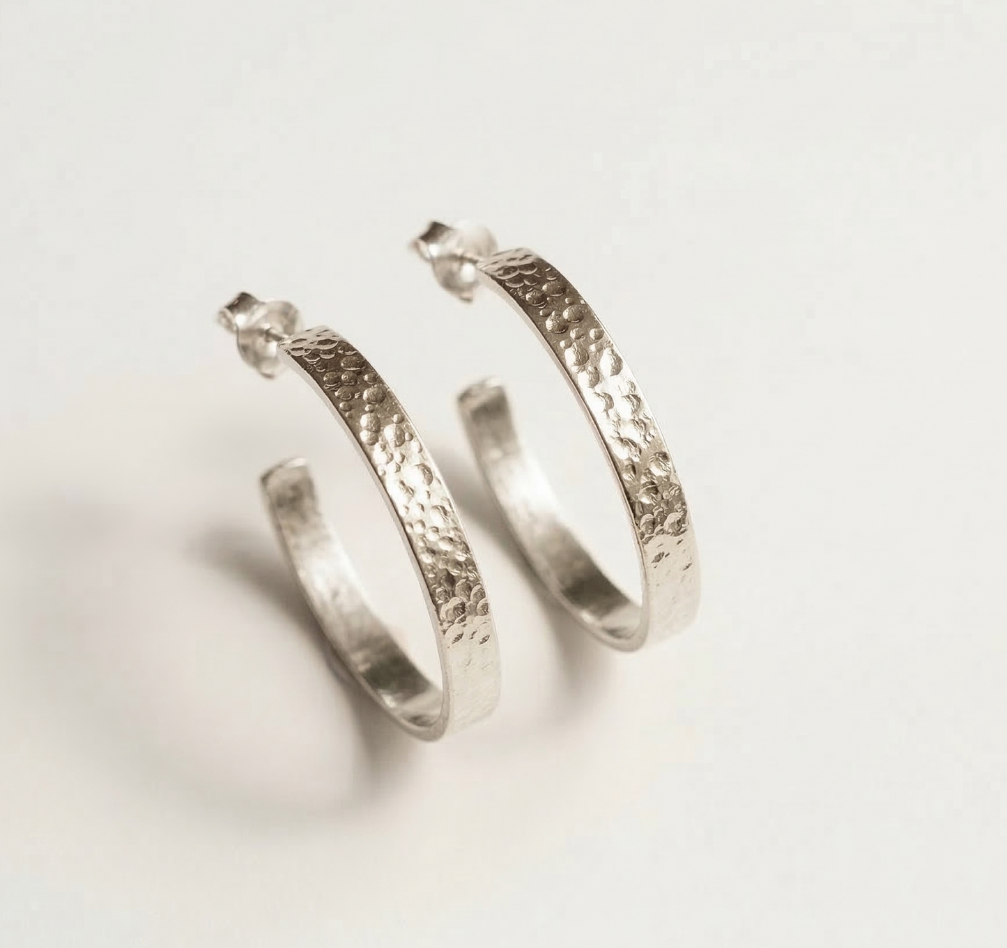Pair of silver hoop earrings with textured design on a light gray background