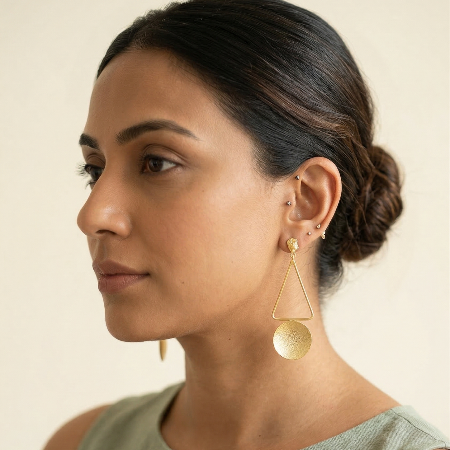 Woman wearing gold earrings against a neutral background