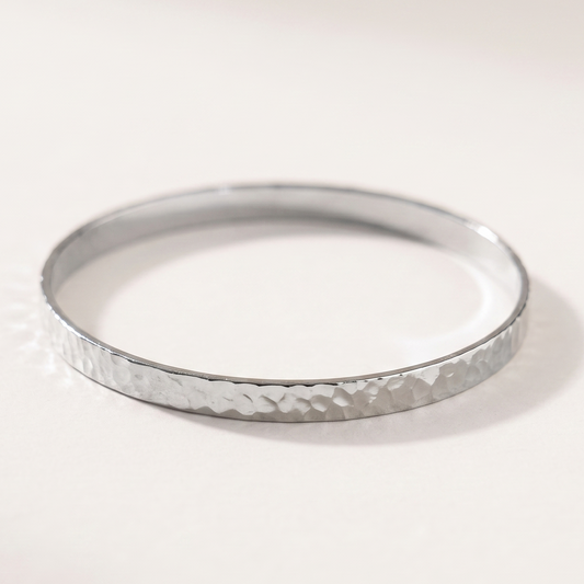 A silver hammered metal bangle bracelet on a clean, light off-white background.