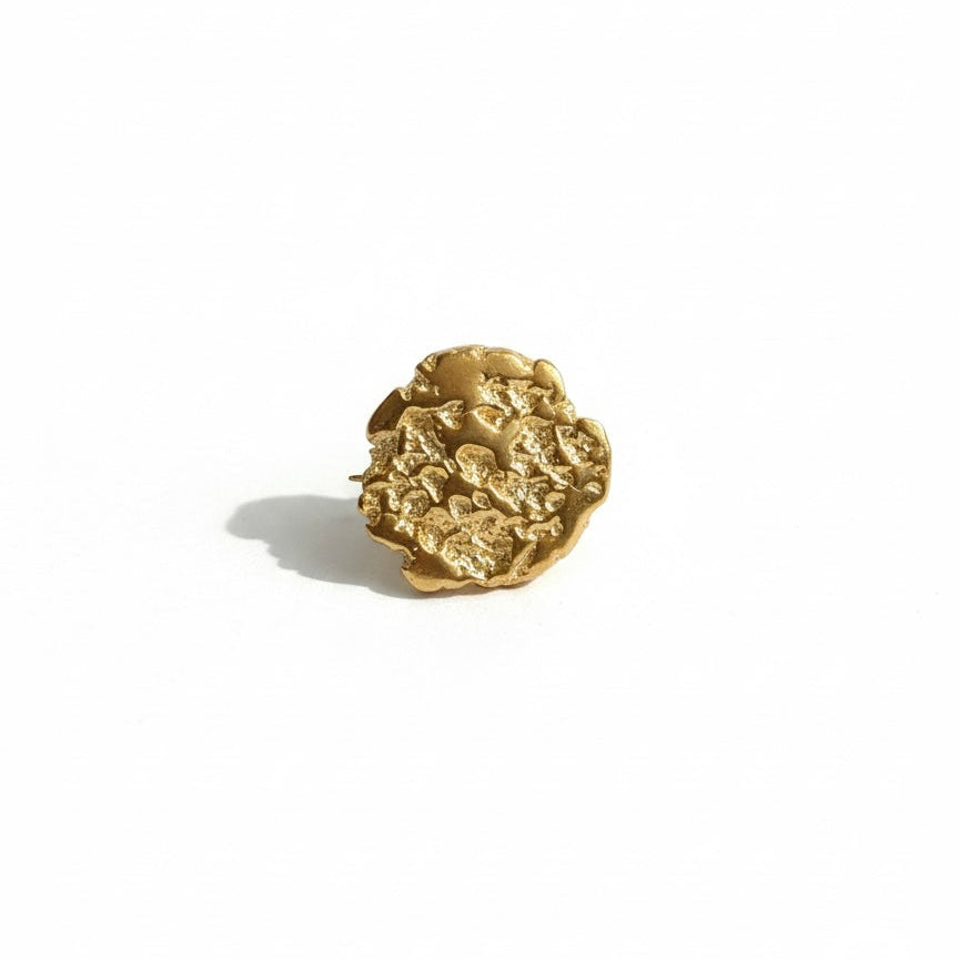 Gold brooch with hammered design on a white background