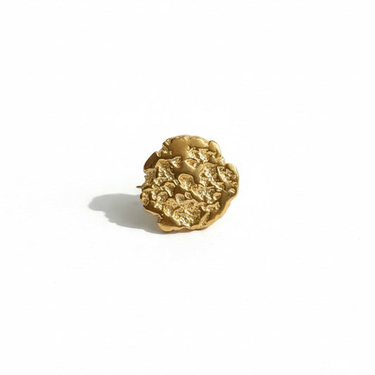 Gold brooch with hammered design on a white background
