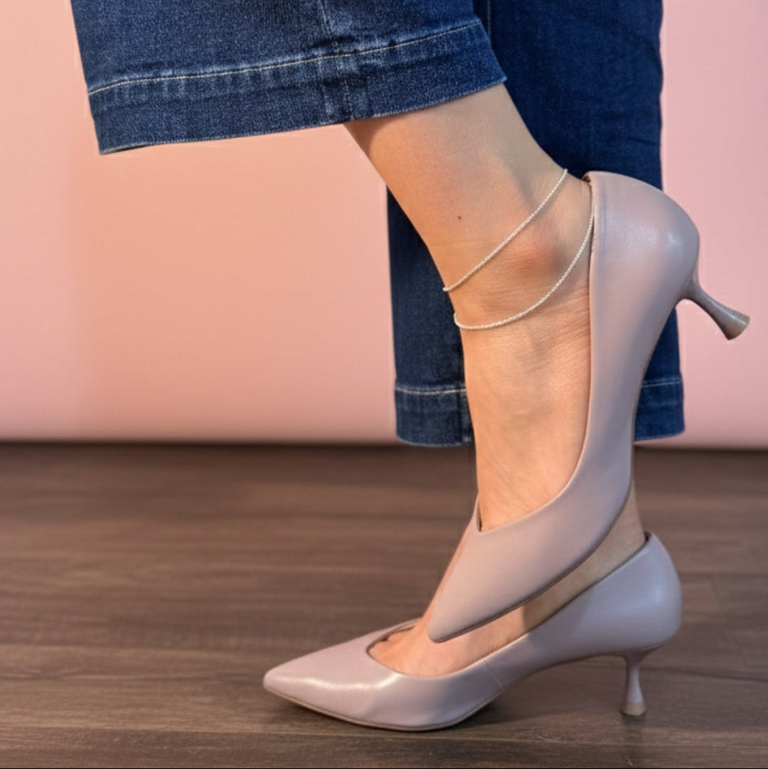 Light gray high-heeled shoes worn with blue jeans on a wooden floor.