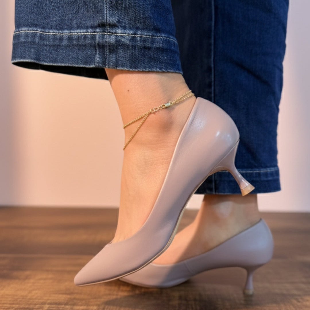 Light pink high-heeled shoes worn with rolled-up jeans on a wooden floor.