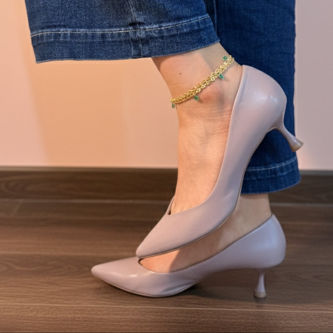 White high-heeled shoes worn with rolled-up jeans on a wooden floor.