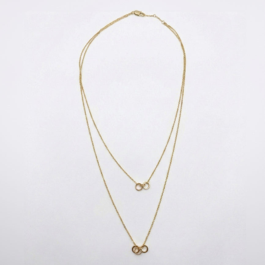 Gold necklace with two interlocking rings on a white background