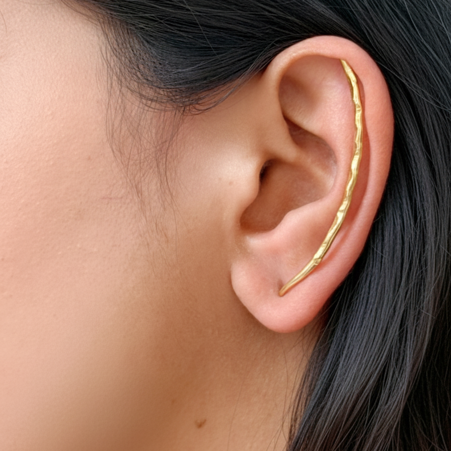 Gold ear climber worn on an ear with a blurred background