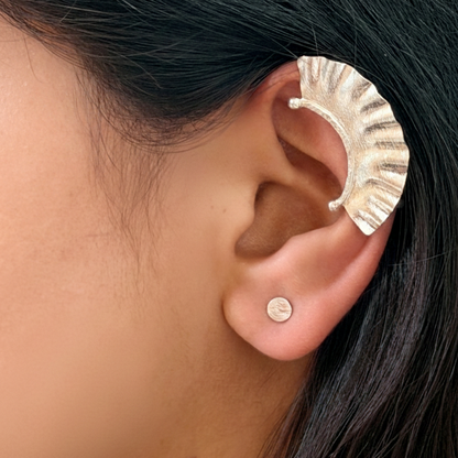 Close-up of an ear wearing a silver ear cuff with dark hair and skin background