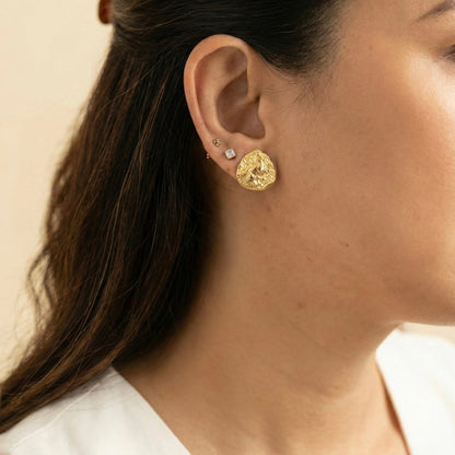 Close-up of a person wearing gold earrings with a neutral background