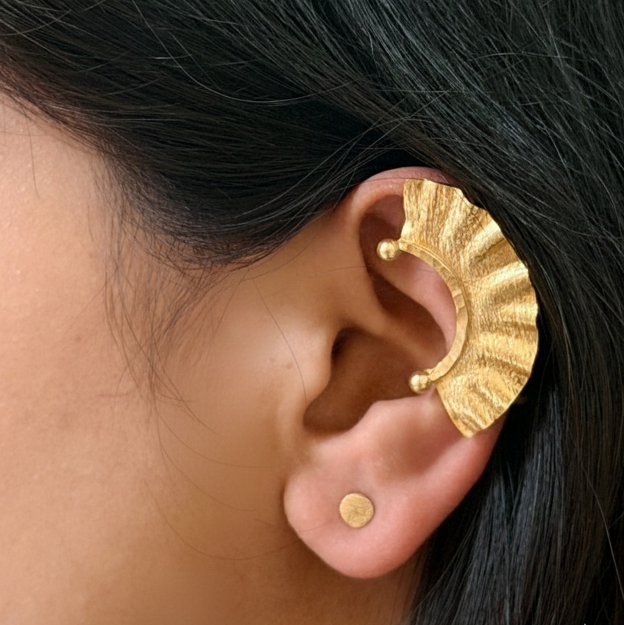 Gold earring worn by a person with dark hair