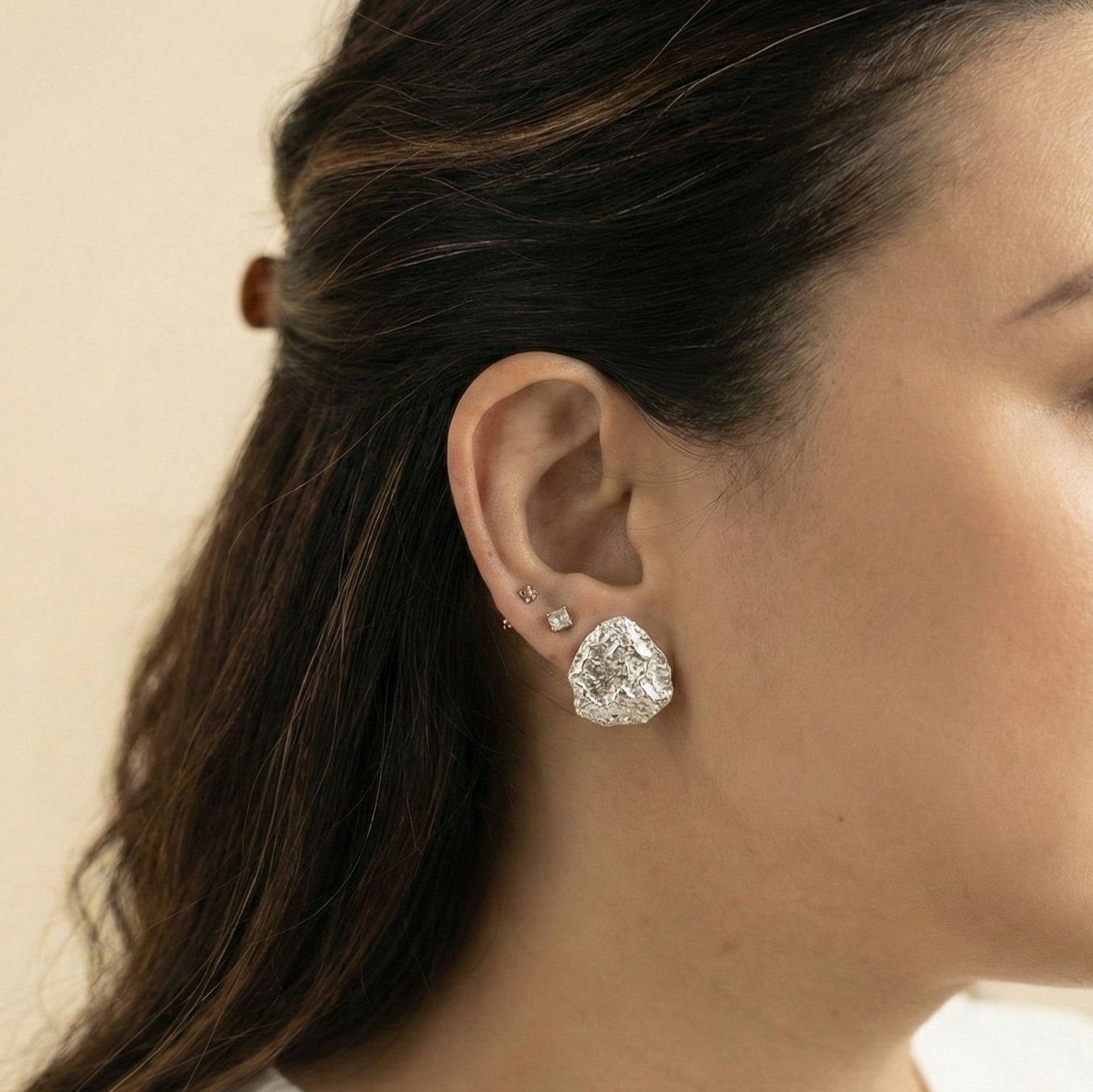 Woman wearing a silver stud earring on a beige background