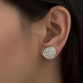 Close-up of a person wearing a silver earring with a textured design.