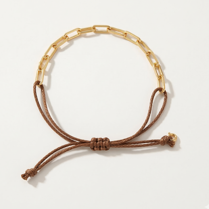 Gold paperclip chain bracelet with a brown cord on a white background