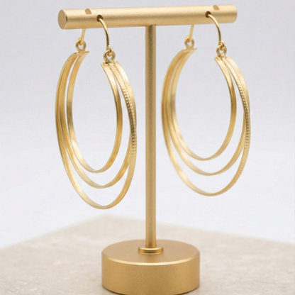 Gold hoop earrings on a gold earring stand against a light gray background