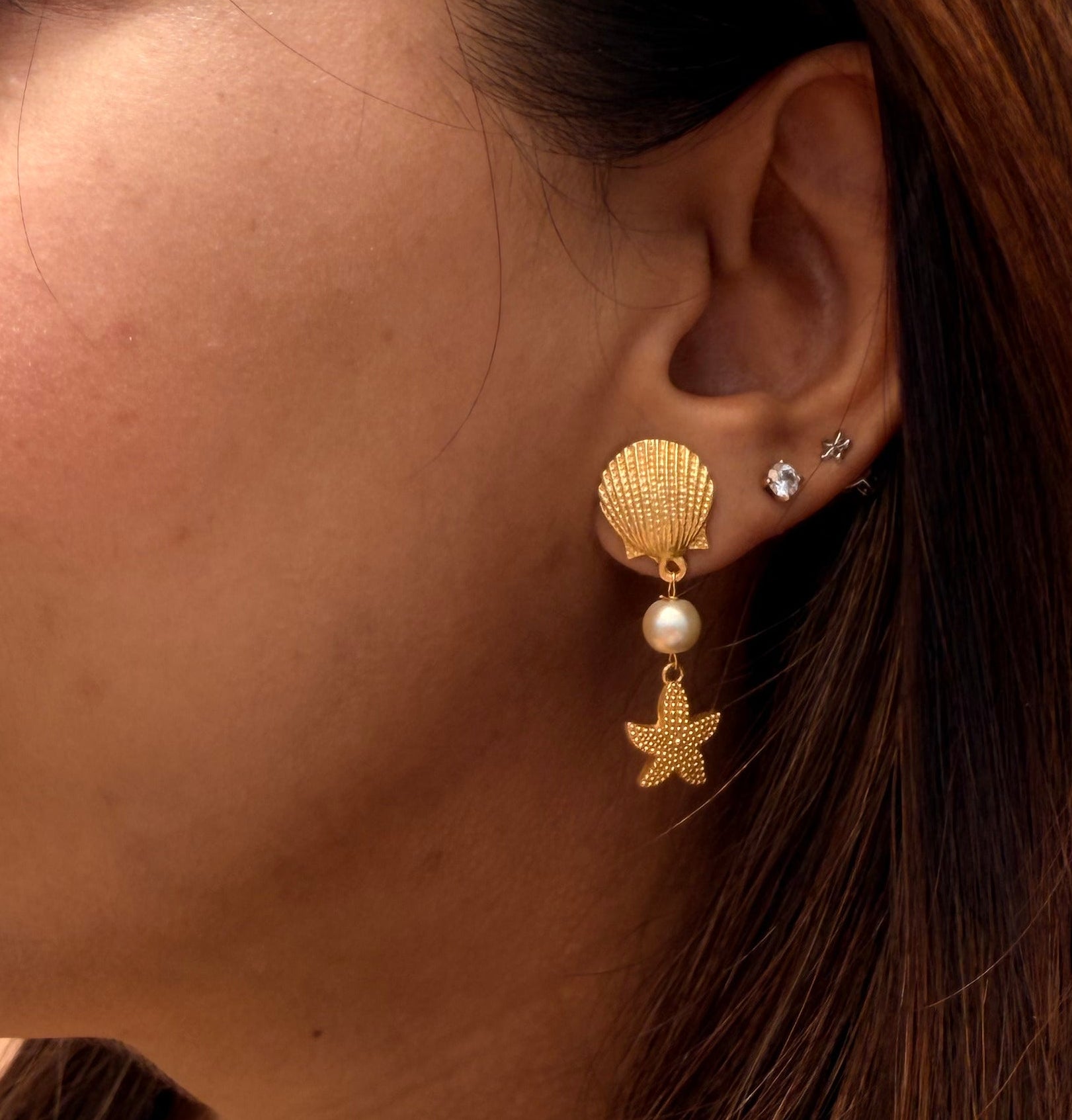 Close-up of a woman wearing gold earrings with pearl shell and star