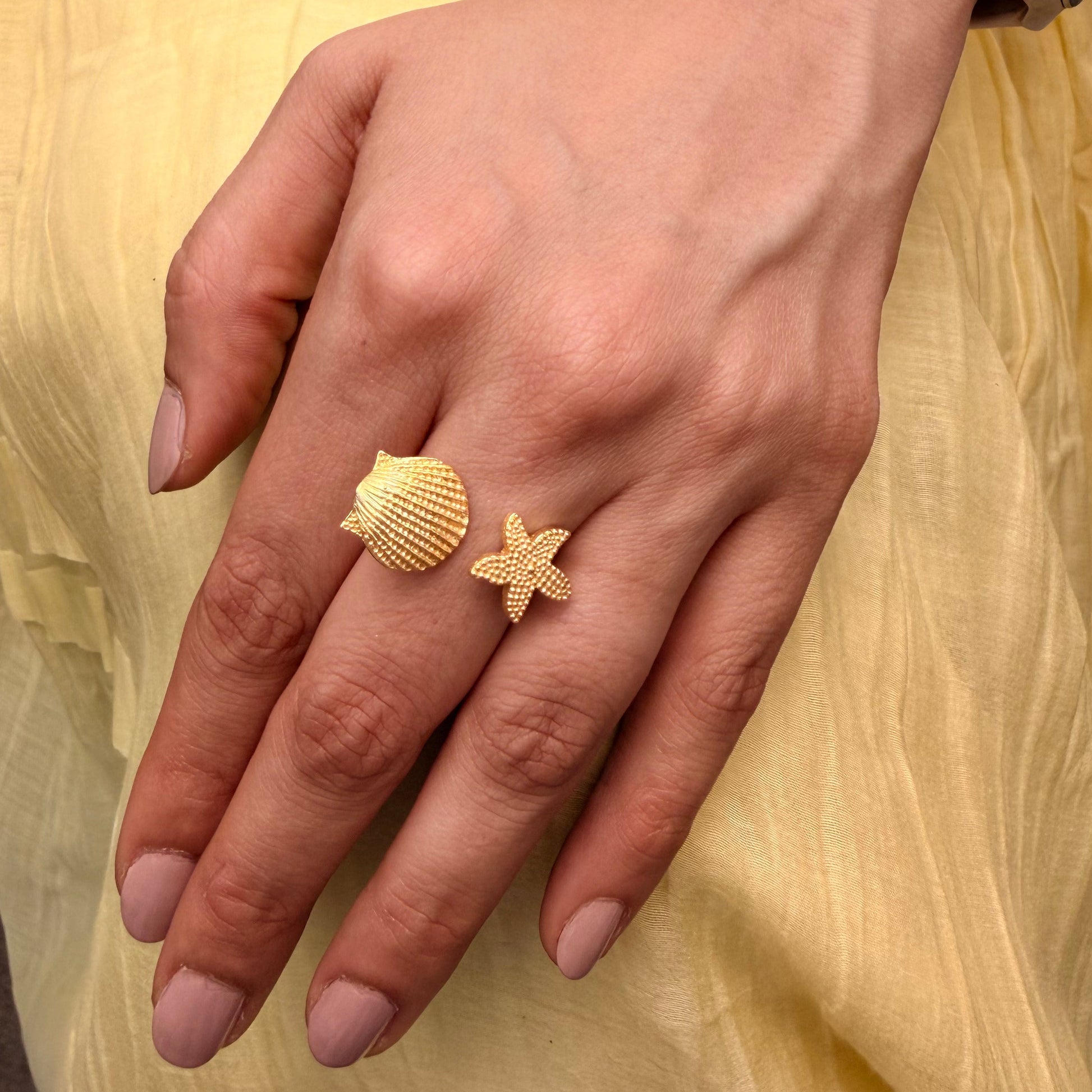Hand wearing gold ring with starfish and shell