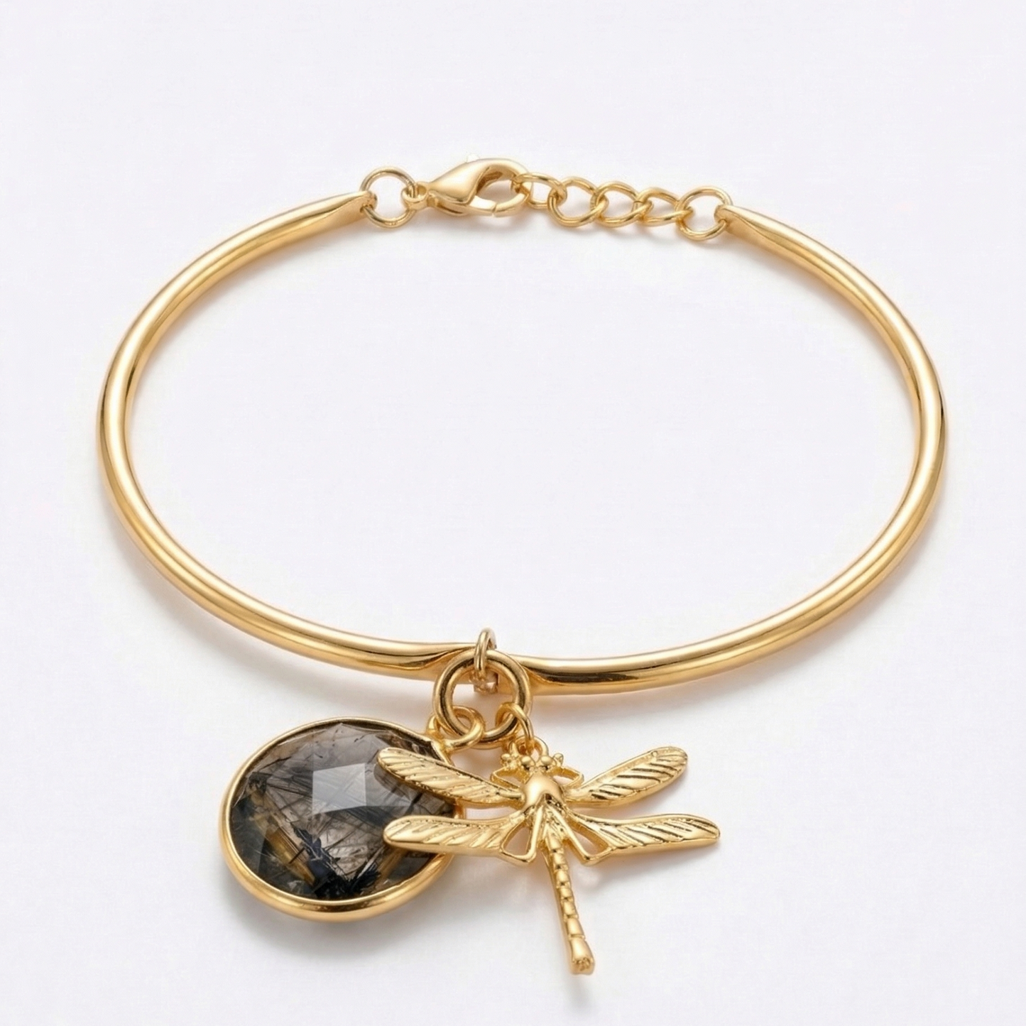 Gold bracelet with a dragonfly charm and round black rutile stone on a white background
