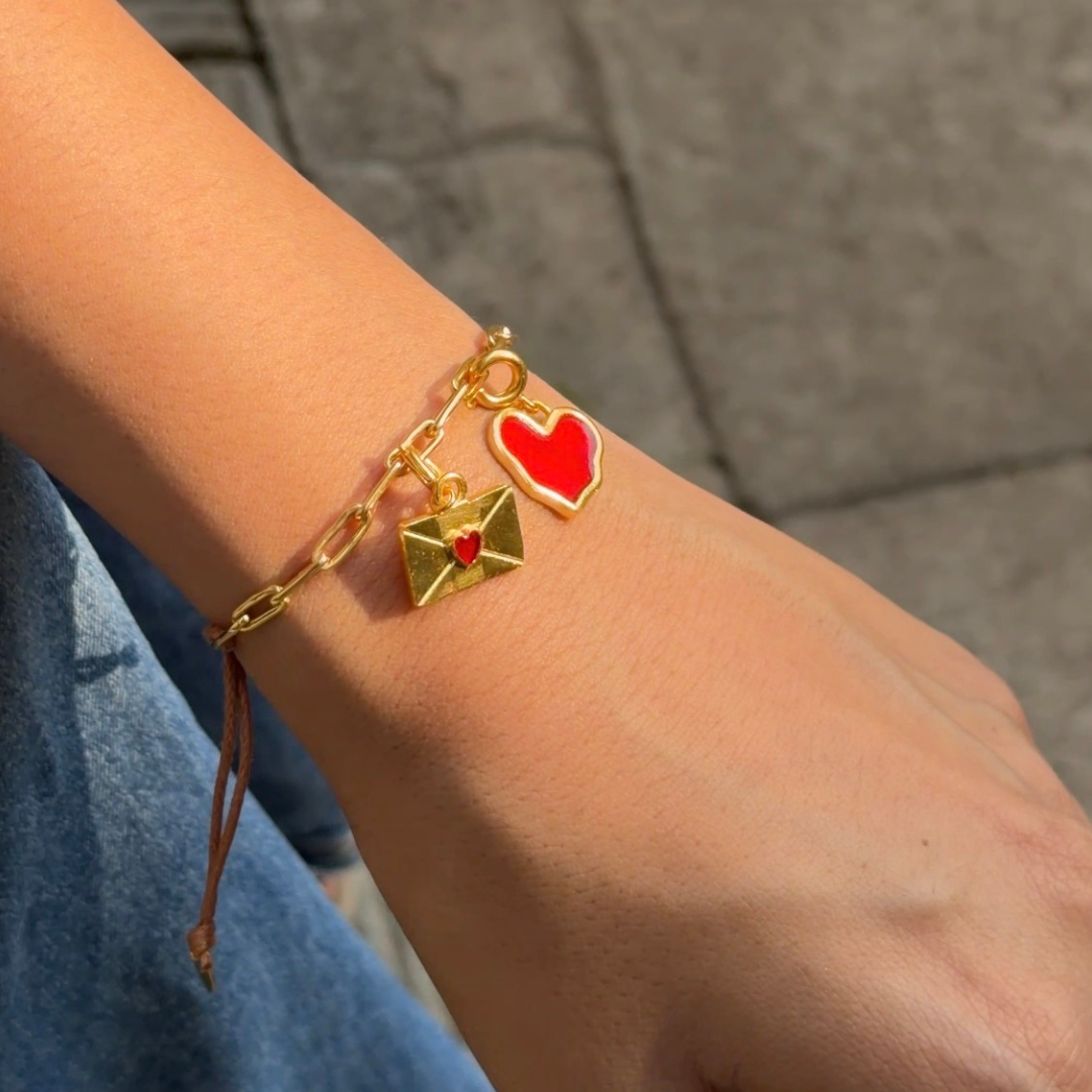 Gold bracelet with heart and letter charms on a wrist against a blurred background