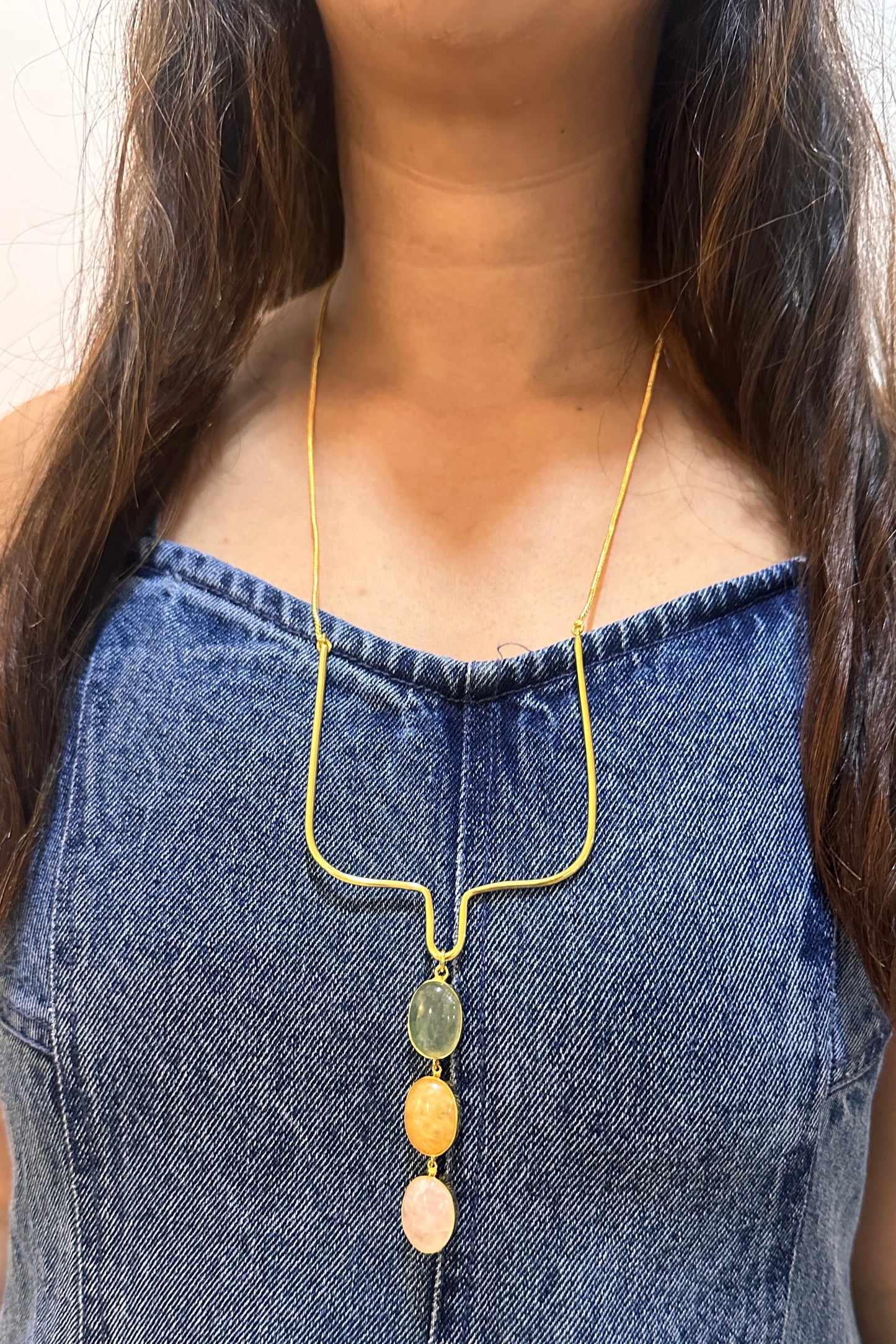 Person wearing a gold necklace with colorful beads against a white background