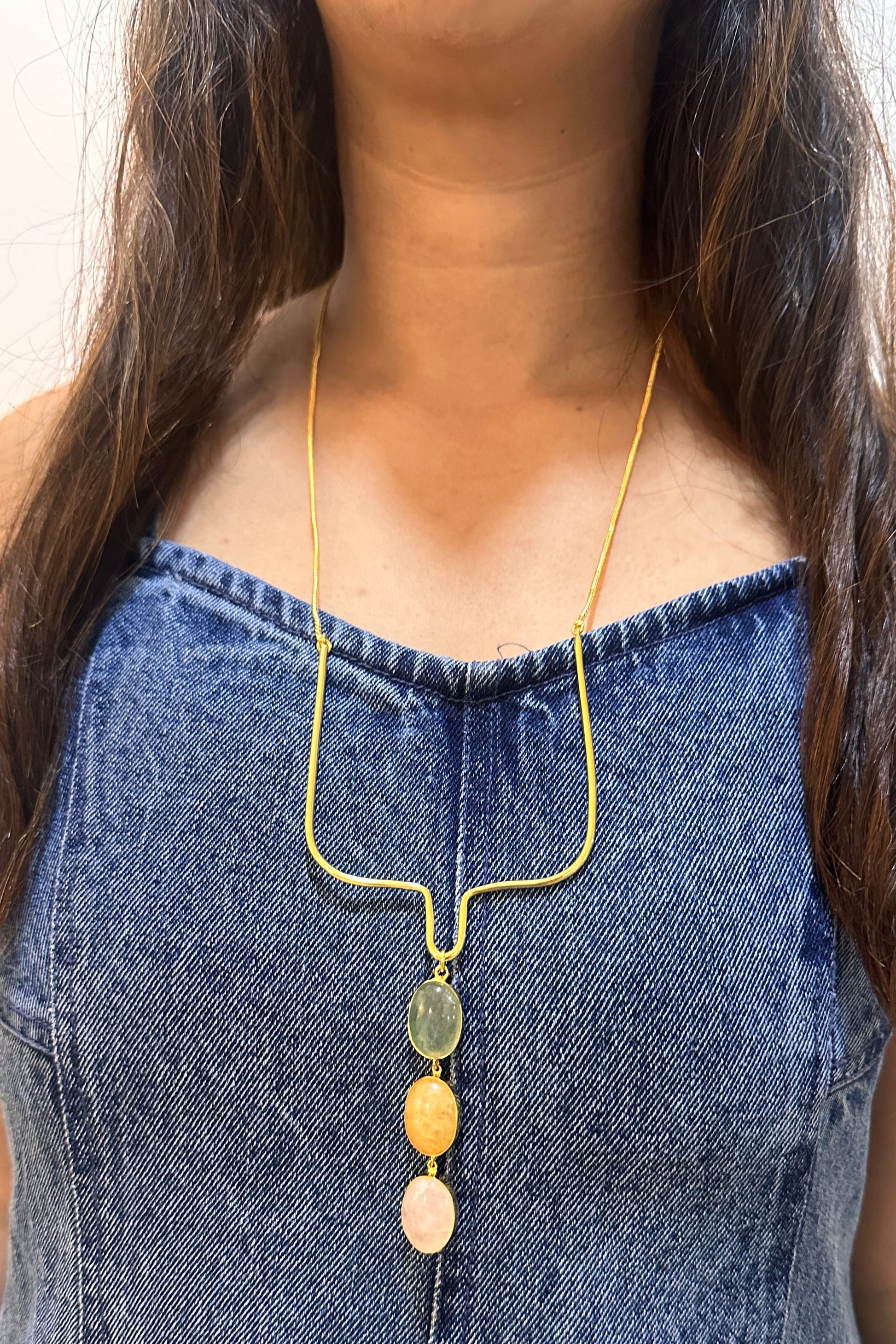 Person wearing a gold necklace with colorful beads against a white background