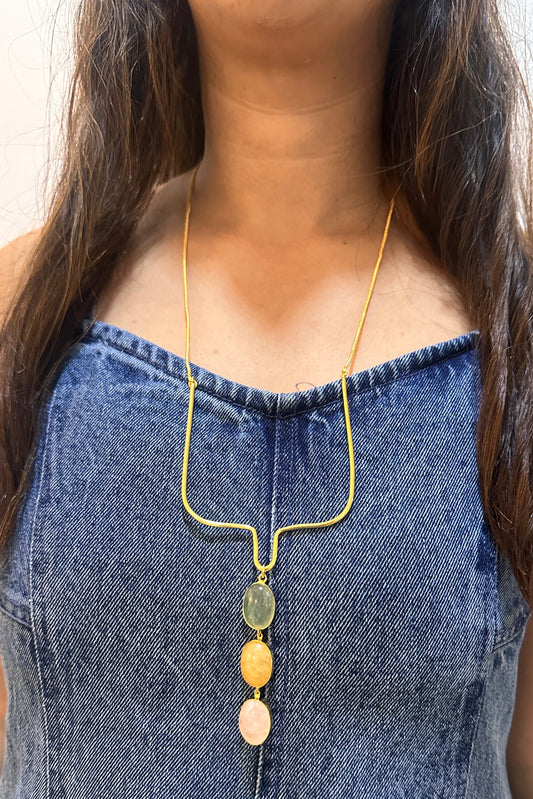 Person wearing a gold necklace with colorful beads against a white background